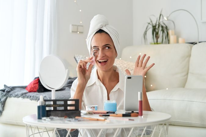 Delighted female with eyelash curler and phone