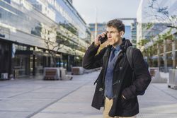 A handsome businessman is talking on the cell phone near his office. Copy space