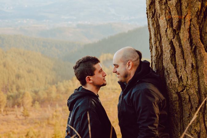 Smiling men hugging near tree in forest on hill