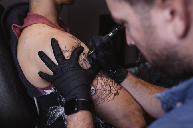 Master doing tattoo on forearm of male customer