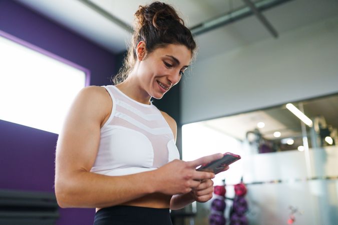 Woman looking down and smiling at her smart phone in gym