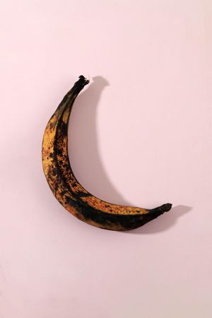 Banana with brown spots on pink background