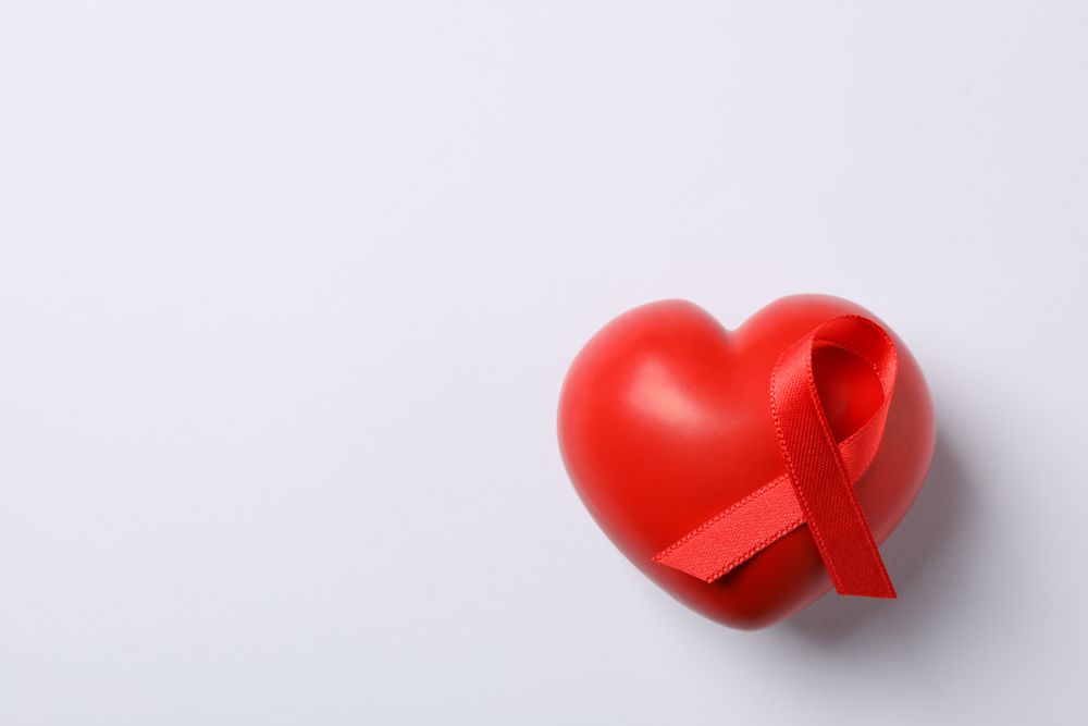 AIDS awareness red ribbon and heart on blank background, space for text