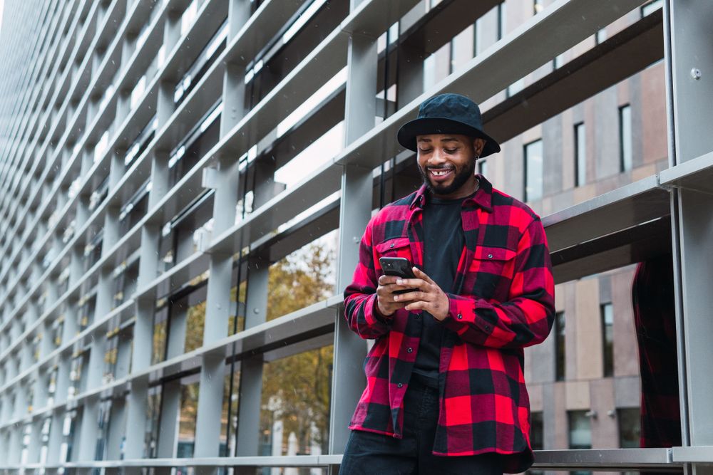Cheerful Black male with smartphone in contemporary building