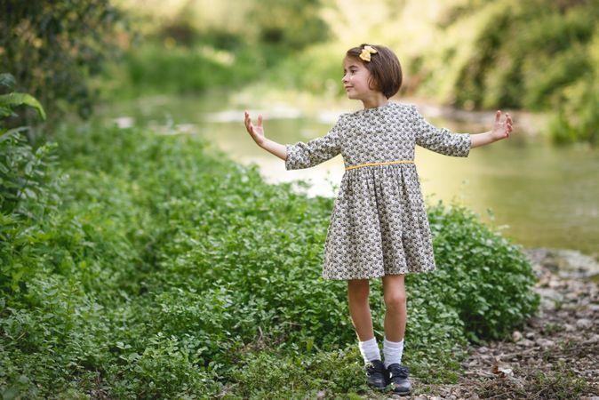 Girl in dress looking away from the river with her arms open