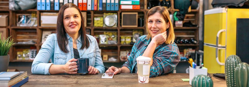 Banner of two smiling female entrepreneurs looking at camera behind of counter in motorbike shop