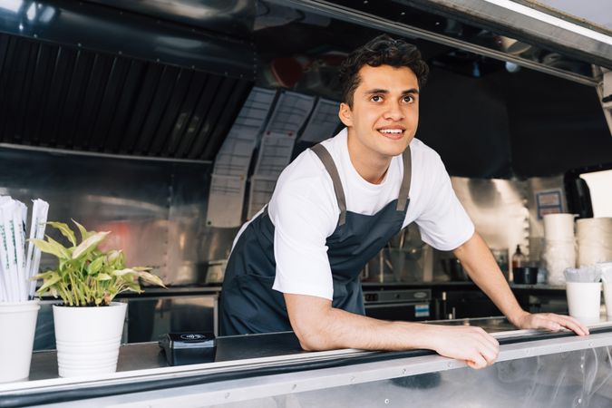 Proud male food truck vendor looking out of van from kitchen