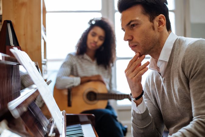 Man playing piano near woman playing guitar in studio