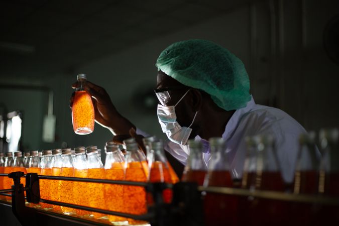 A factory worker is holding a bottle of fruit juice to inspect its quality inside a beverage manufacturing facility.