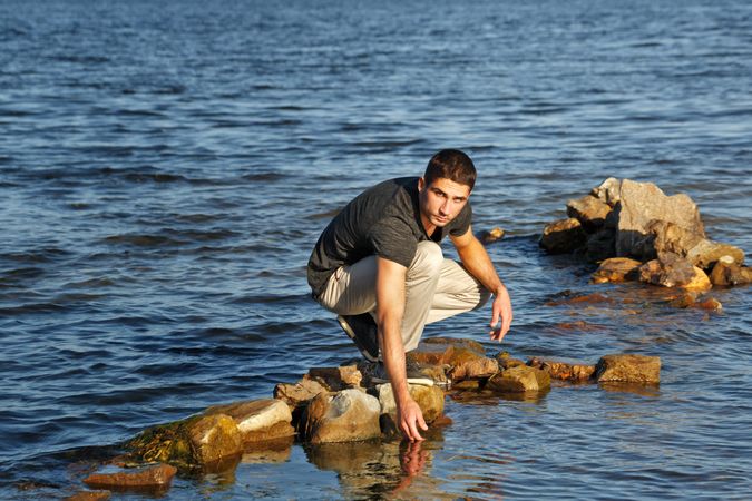 Male sitting down on rocks touching lake water