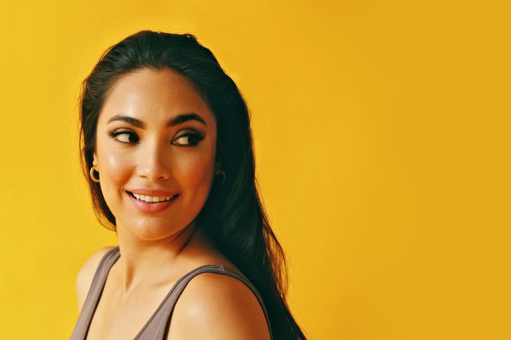 Headshot of Hispanic woman with head looking behind her on yellow background