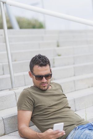 Man reclining on outdoor stairs while texting on phone, vertical