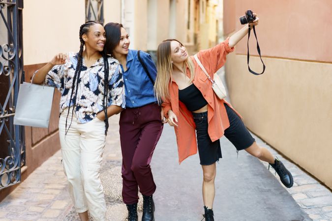 Three happy women walking down narrow lane and taking photos with camera