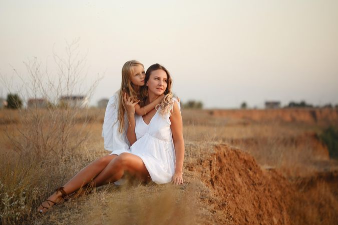Adult female and child in summer dress relaxing on top of cliff at dusk