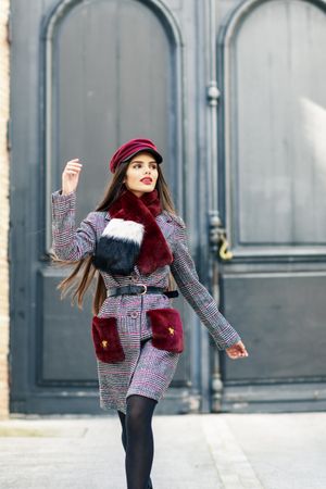 Confident woman standing in winter clothes walking in front of outside door looking in distance