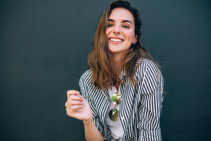 Happy looking woman with striped shirt standing against a wall posing for photograph