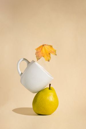 A stacked pear, mug and autumn leaf