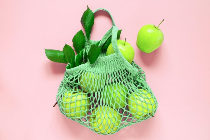 Mesh bag of bright green apples on pink background