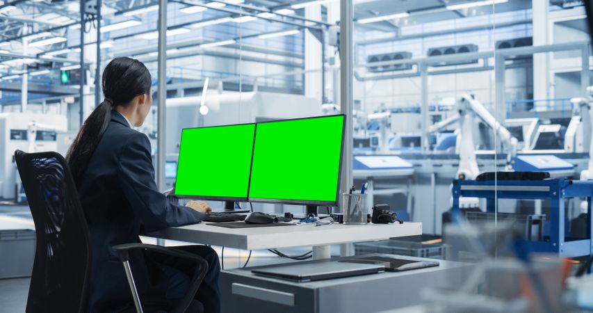 Female Robotics Technician Working on a Desktop Computer with Green Screen Chromakey Mock Up Display in a Factory Office. Technological Research and Development Facility with Autonomous Assembly Line