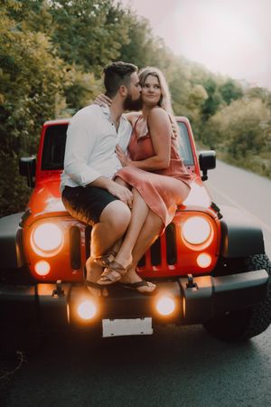Loving couple sitting on car on road near forest