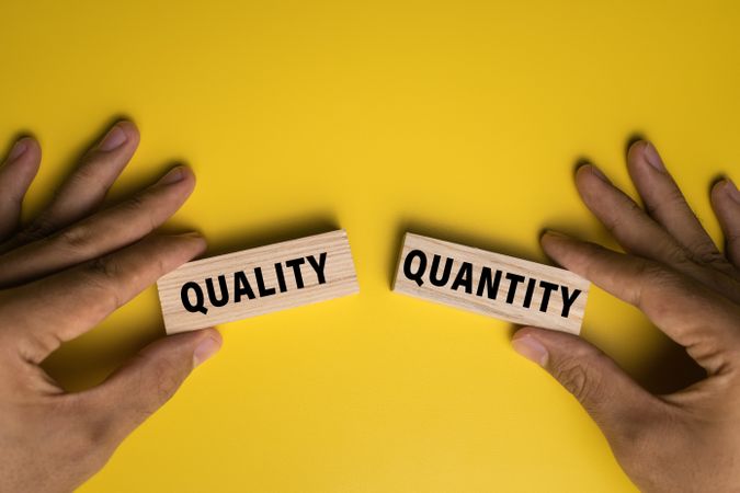 male hand holding quality and quantity words on wooden blocks isolated on yellow background