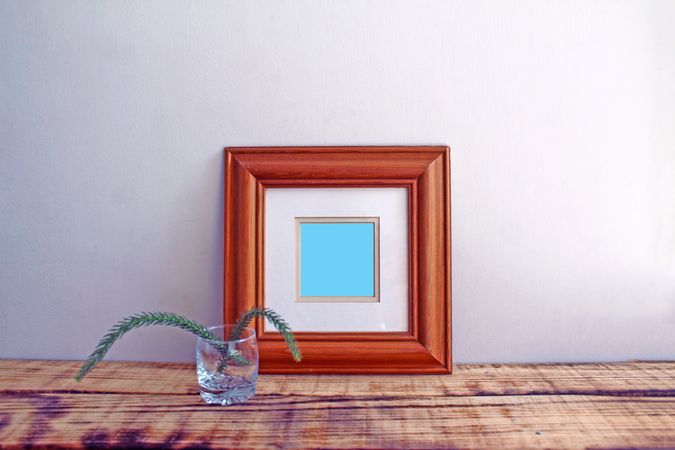 Square wooden picture frame on wooden desk with branch mockup