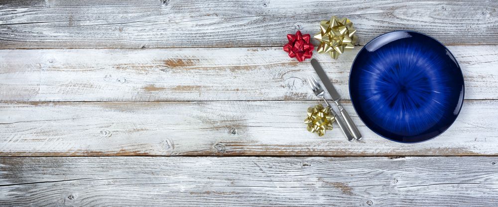 Basic table setting of an empty main dark blue dish with cutlery on wood plus holiday decorations