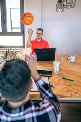 Businessman in brainstorm having fun throwing a basket ball to colleague in office