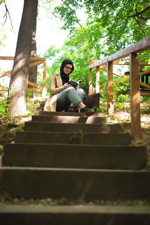 Woman sitting at the top of forest stairs with a book