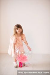 Girl in pink dress holding a balloon against light background 5lwda0