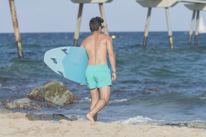Male surfer with blue board approaching the sea