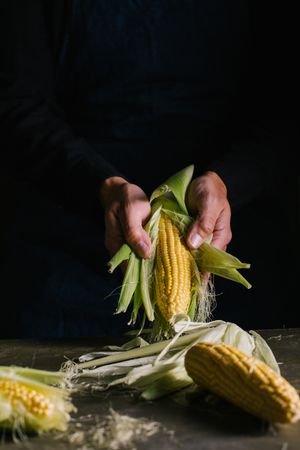 Crop person peeling corn over table