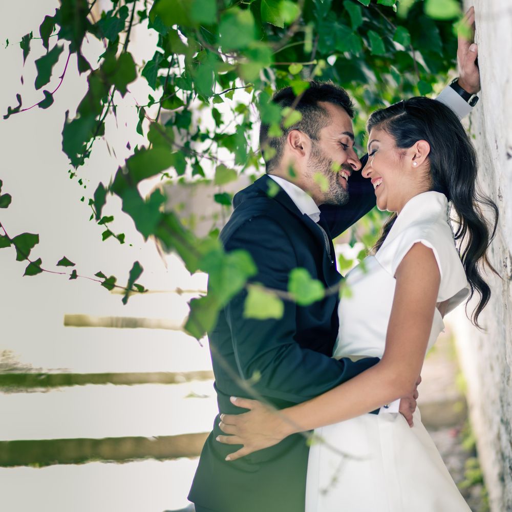 Happy newlywed couple facing each other under bright green branches