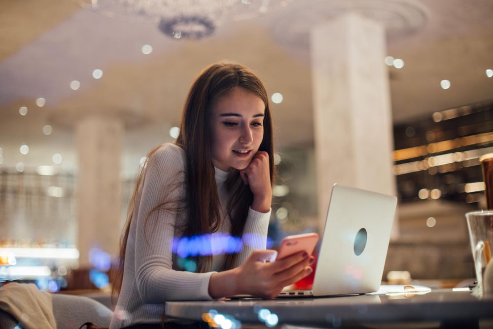 Young woman texting in a cafe with laptop in front of her