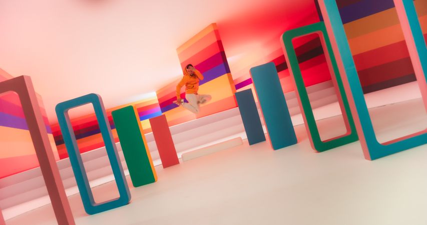 Male Dancer in Bright Sweater Performing Swift Breakdancing Moves in a Colorfully Decorated Studio. Professional B-Boy Showcasing his Talent and Skills, Surrounded by Stylish Geometric Decoration