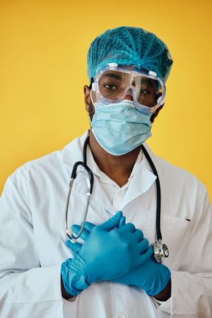 Closeup portrait of Black medical doctor in yellow studio with full ppe gear, and stethoscope