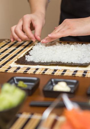 Hands of woman chef preparing sushi rolls with rice on a nori seaweed sheet, vertical