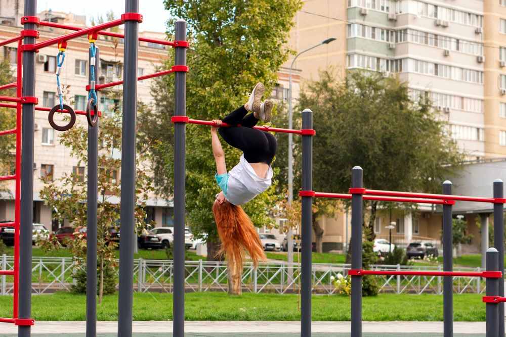 Woman performing gymnastic trick on outdoor horizontal bar in park.