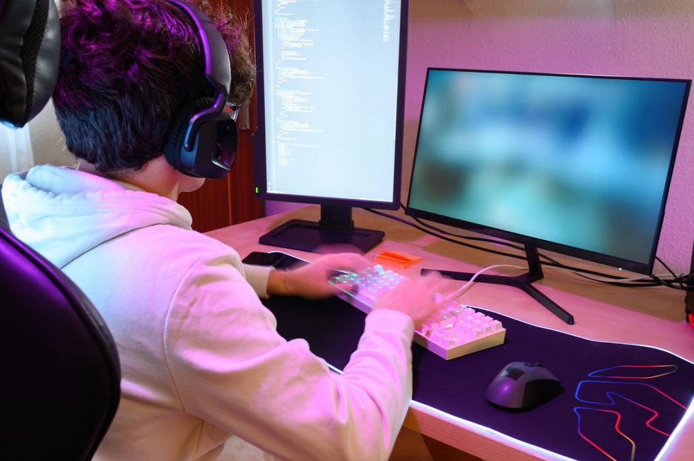 Anonymous young man in headphones playing on keyboard and sitting at table with gadgets