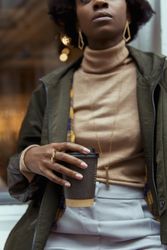 Close-up shot of Black woman in green jacket holding a cup of coffee