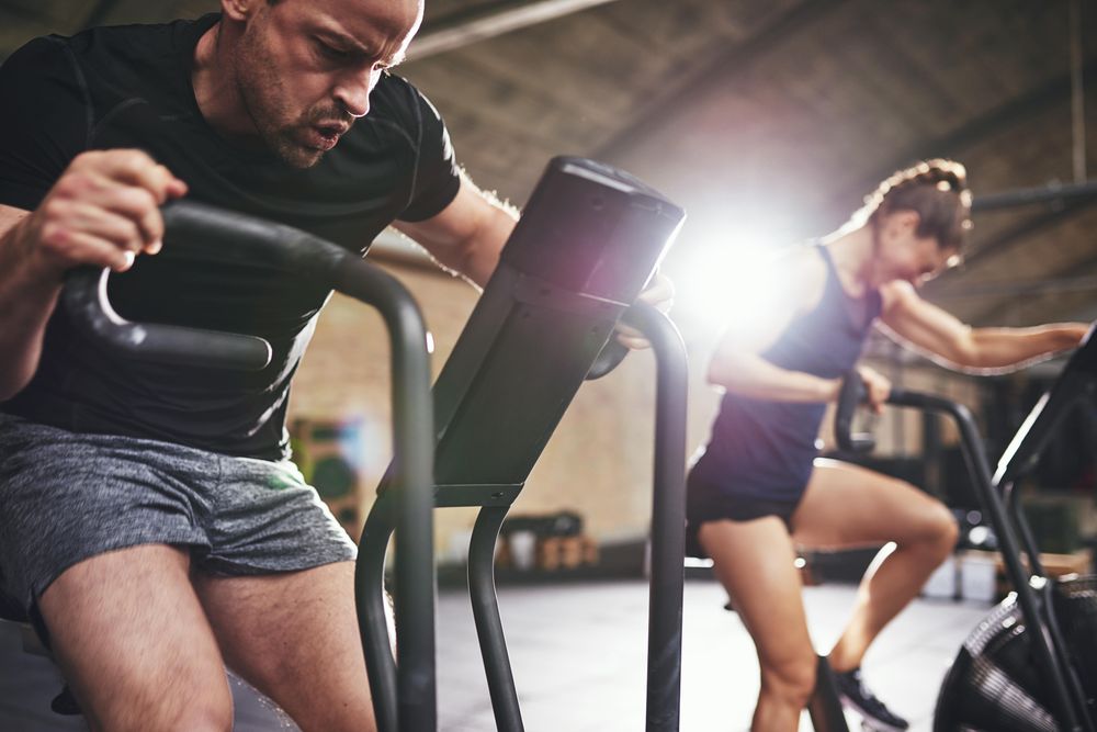 Two adults concentrating on speed and time while on exercise bikes