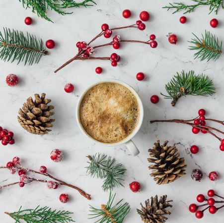 Pattern made of pine cones, pine needles, and holly berries surrounding coffee cup