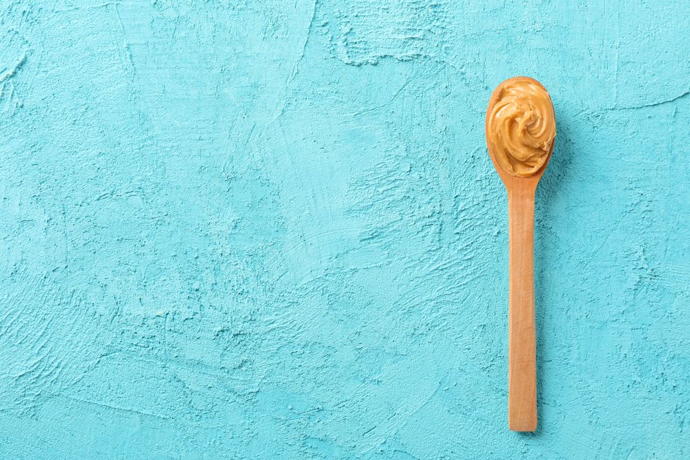 Spoon with peanut butter on color background, space for text and top view