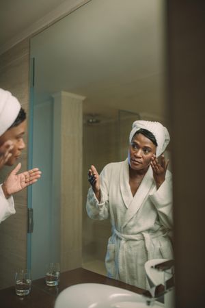 Woman in bathrobe applying cosmetic lotion to take care of the skin in the bathroom