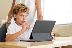 Smart boy using tablet during lesson with crop teacher