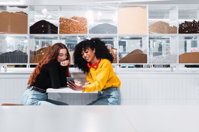 Positive multiethnic female friends using smartphone and laughing in cafe