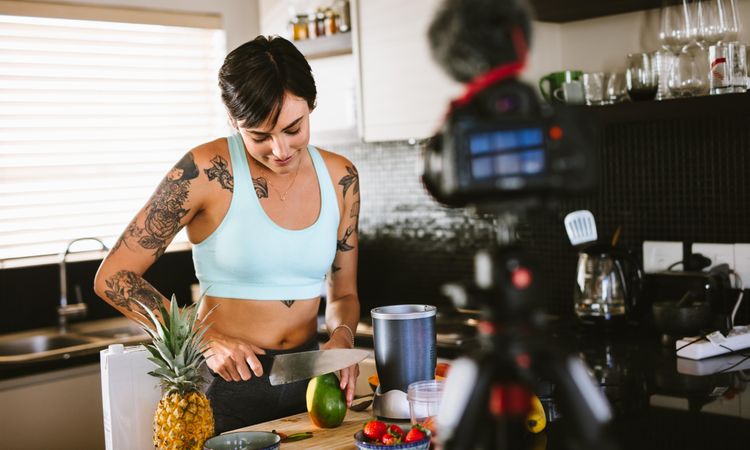 Social media influencer in kitchen making smoothies and recording content for her video blog