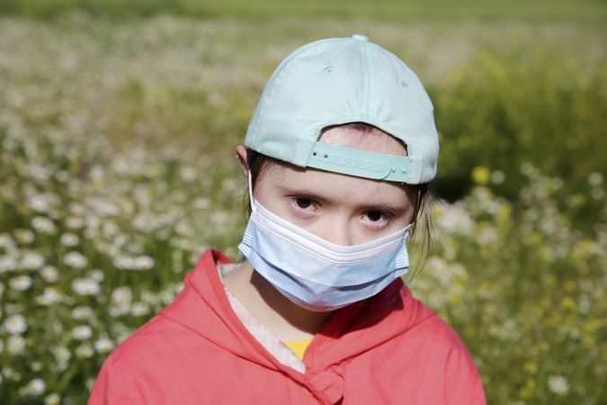 Child wearing medical mask over face outdoors in a garden