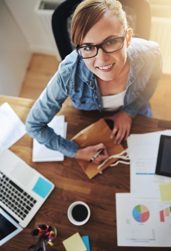 Top view of smiling female looking up while at labeling a bag at her desk
