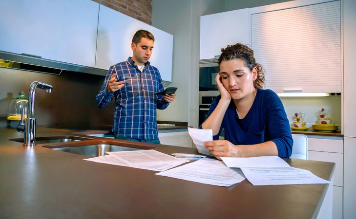 Man and woman looking dismayed about bills scattered on kitchen counter